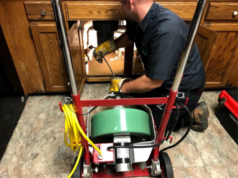 A man using a cable machine to open a clogged kitchen sink line.